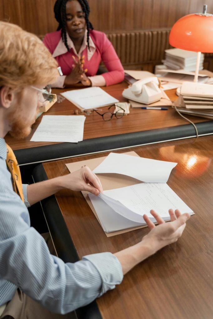 Two professionals in a focused meeting at an office desk, reviewing documents.